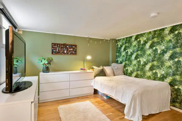 Chambre avec mur végétal, lit blanc, commode et télévision.
