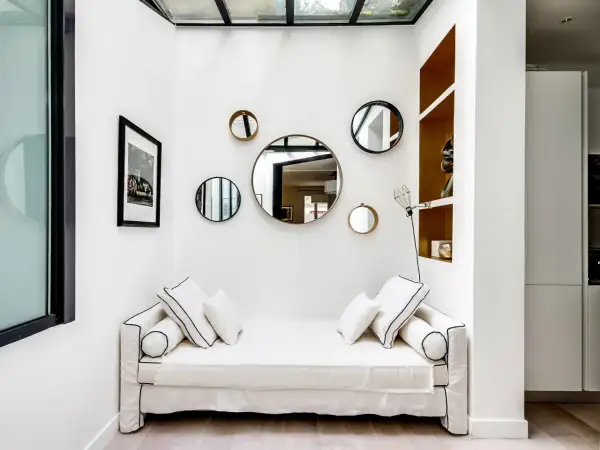 Plusieurs miroirs ronds de tailles variées sont accrochés sur un mur blanc au-dessus d'un canapé blanc.