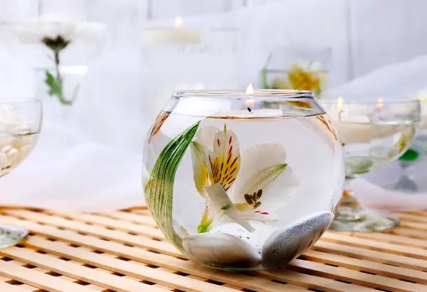 Comment décorer un grand vase en verre transparent : une fleur blanche flottante, des galets et une bougie allumée créent une ambiance zen.