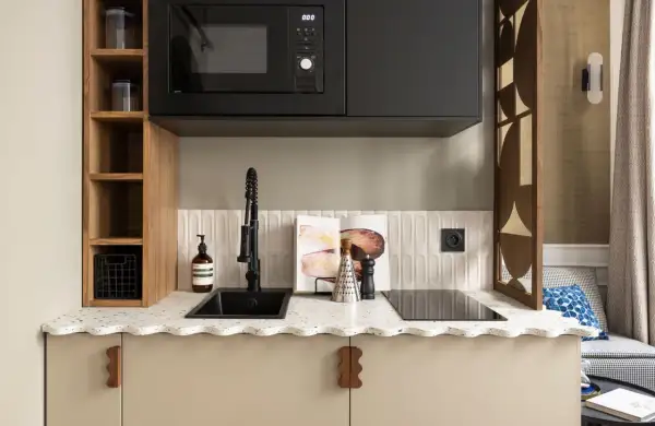 Petite cuisine moderne avec évier noir, plaque de cuisson, micro-ondes et étagères en bois.