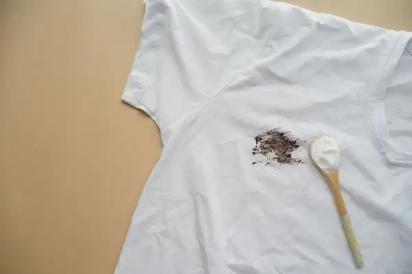 Tache de gras sur un t-shirt blanc, avec une cuillère de poudre blanche prête à enlever la tache de gras sur tissu.