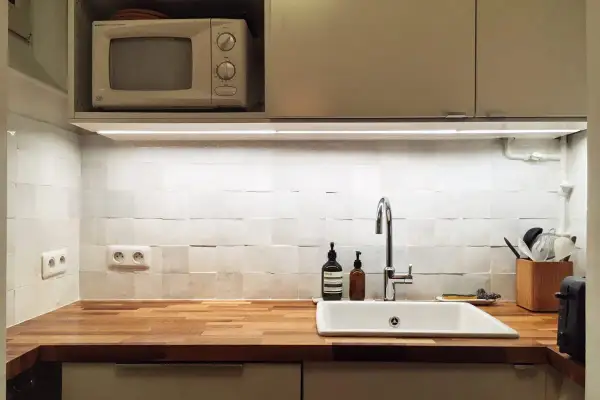 Cuisine blanche épurée avec crédence en zellige texturé, plan de travail en bois, évier et robinetterie modernes.