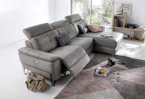 Canapé d'angle gris en cuir, avec repose-pieds déployé. Ce fauteuil relax qui grince est prêt pour un moment de détente.