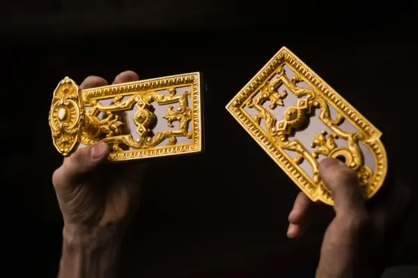 Mains tenant des ornements dorés, peut-être du bronze ou du laiton, aux motifs complexes.