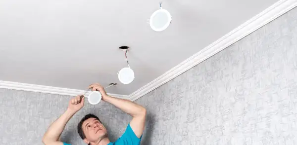 Un homme installe de nouvelles suspensions rondes au plafond, remplaçant les anciens spots.