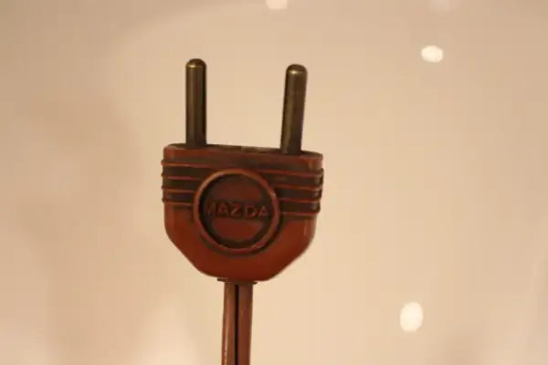 Prise électrique ancienne en bakélite marron avec le logo Mazda. Pour savoir comment reconnaître une lampe Mazda, cherchez cette marque distinctive.
