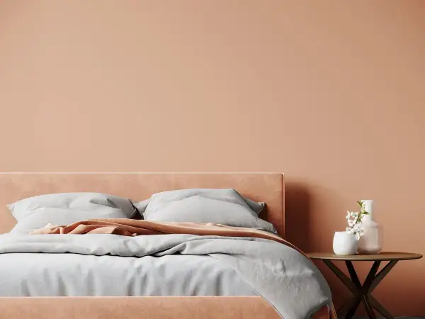Lit douillet dans une chambre aux tons pêche, une belle idée couleur chambre adulte zen. Draps gris, plaid corail et vase fleuri sur table ronde.