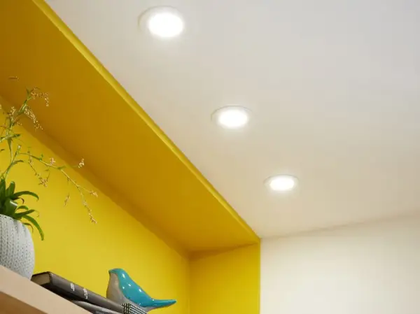 Disposition de spots encastrés au plafond pour une ambiance lumineuse dans la chambre, éclairant joliment les étagères jaunes.