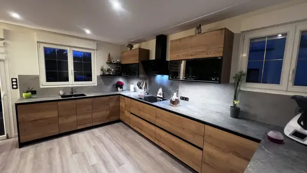 Cuisine moderne avec meubles en bois, plan de travail gris et hotte noire.