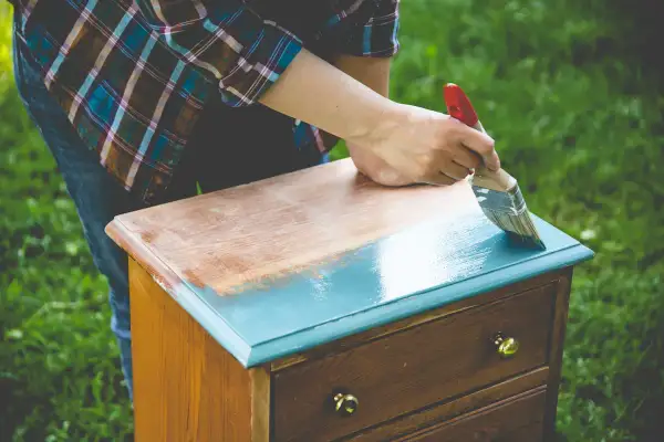 Une personne ponce un meuble vernis pour le repeindre en bleu sarcelle.