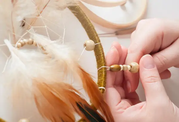 Mains assemblant un attrape-rêves, ajoutant des perles en bois pour une touche naturelle. Idées pour que faire avec des perles en bois.