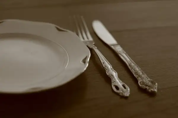 Une assiette blanche et des couverts en argent ornés, prêts pour un repas. Apprenez comment nettoyer des couverts en argent pour qu'ils brillent.