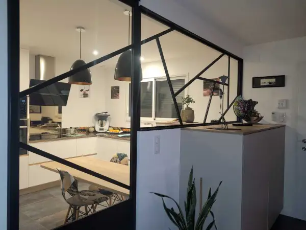 Une cuisine moderne avec une cloison lumineuse en verre et métal noir, séparant l'espace repas de la cuisine.
