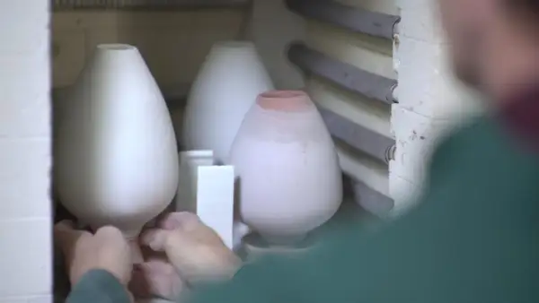 Mains plaçant délicatement des pièces de céramique au four pour leur cuisson.