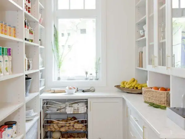 Arrière-cuisine blanche avec étagères remplies, fruits et légumes sur le comptoir.