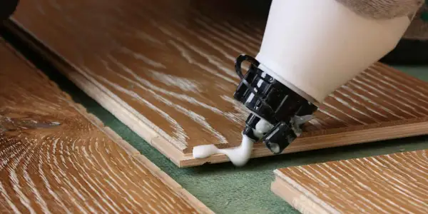Application de colle à bois sur des lames de parquet. La colle blanche coule de l'embout d'une bouteille sur le bois.
