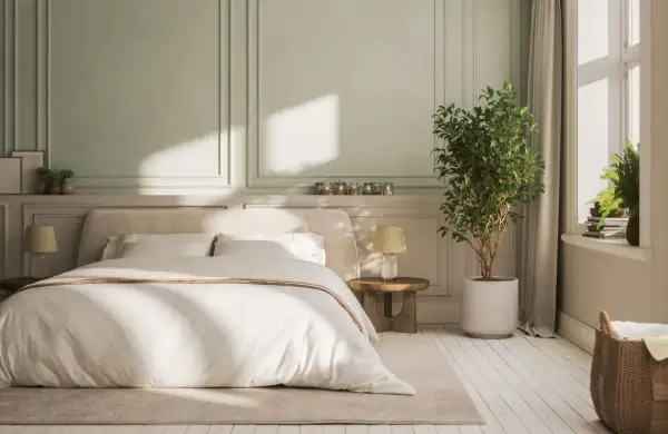 Chambre avec lit blanc, lambris vert pâle et plante verte.