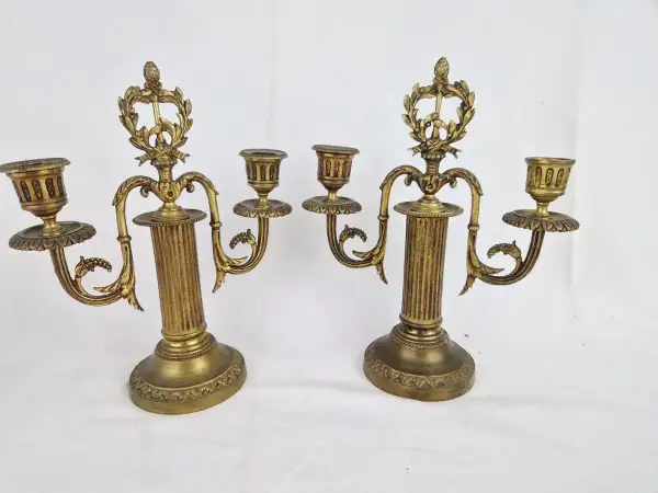 Deux candélabres en bronze doré, ornés de guirlandes et de cannelures, illustrent comment reconnaître un chandelier ancien par leur style et leur patine.