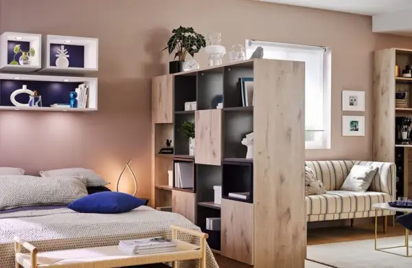 Chambre et salon séparés par une étagère modulable, avec lit douillet et canapé rayé.