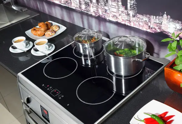 Plaque à induction avec deux casseroles, tasses de café et viennoiseries.