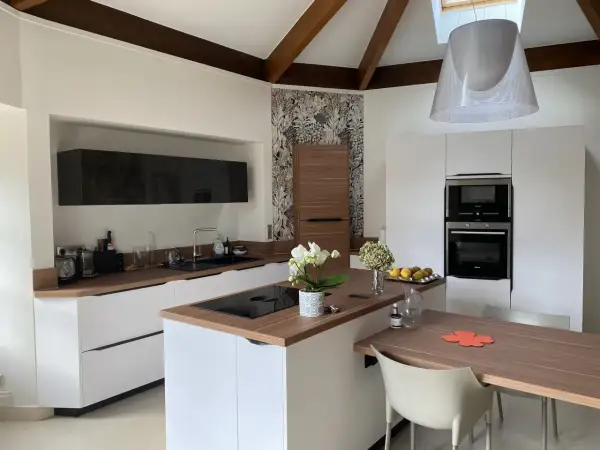 Cuisine moderne avec des meubles blancs et un **crédence et plan de travail assortis** en bois. Une orchidée blanche décore l'îlot central.