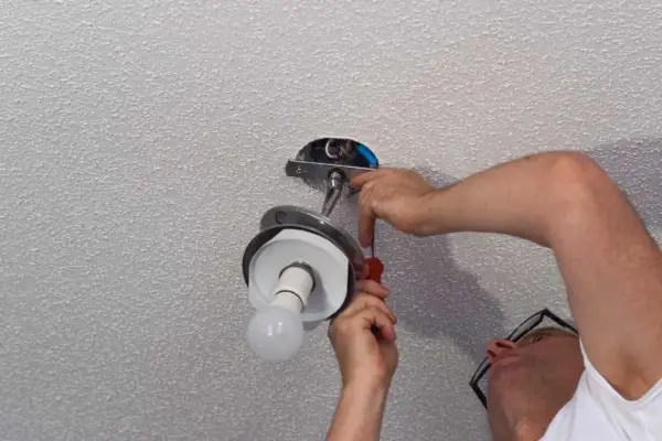 Un homme installe un lustre au plafond, utilisant un tournevis pour fixer le luminaire.