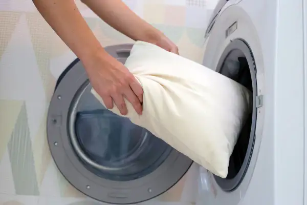 Une personne met un oreiller blanc dans une machine à laver.