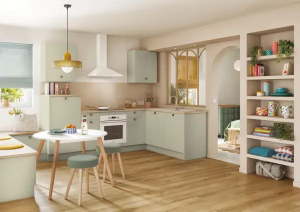Cuisine moderne et colorée avec des meubles verts, une table ronde et des étagères décorées.